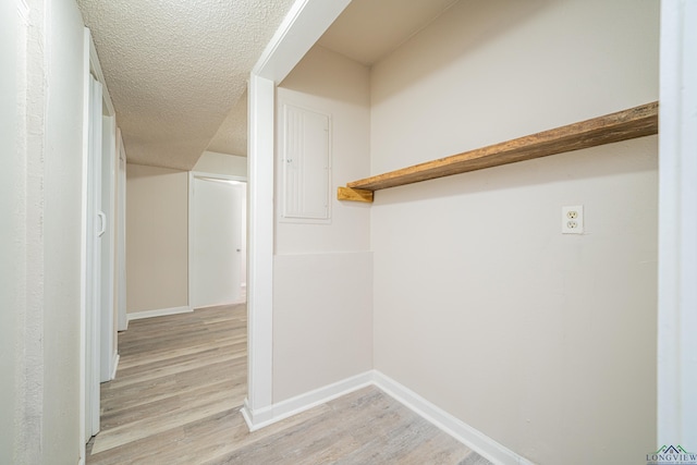 laundry room featuring light wood-style flooring, baseboards, and a textured ceiling