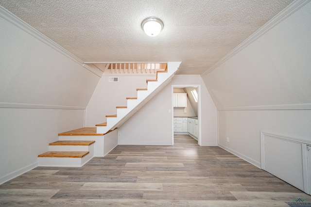 additional living space featuring visible vents, a textured ceiling, wood finished floors, baseboards, and stairs