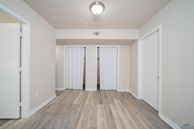 unfurnished bedroom featuring two closets, visible vents, a textured ceiling, light wood-type flooring, and baseboards