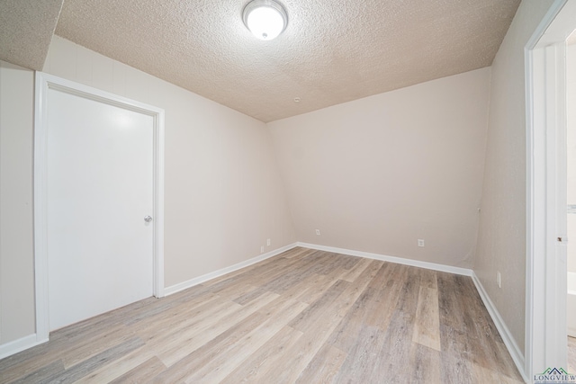 spare room with light wood finished floors, baseboards, and a textured ceiling