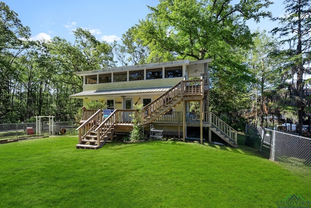 rear view of property featuring a lawn, a sunroom, and a wooden deck