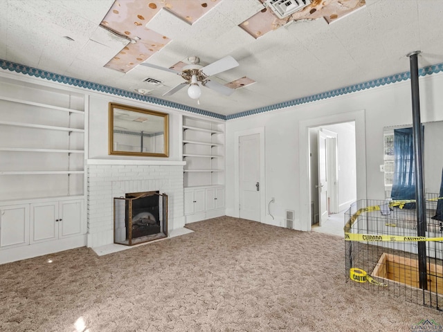 carpeted living room featuring built in shelves, a brick fireplace, visible vents, and a ceiling fan