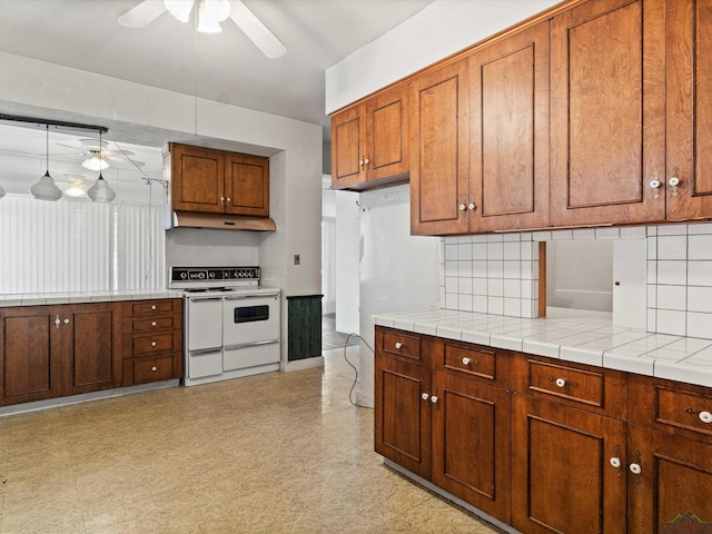 kitchen with range with two ovens, a ceiling fan, brown cabinetry, under cabinet range hood, and backsplash