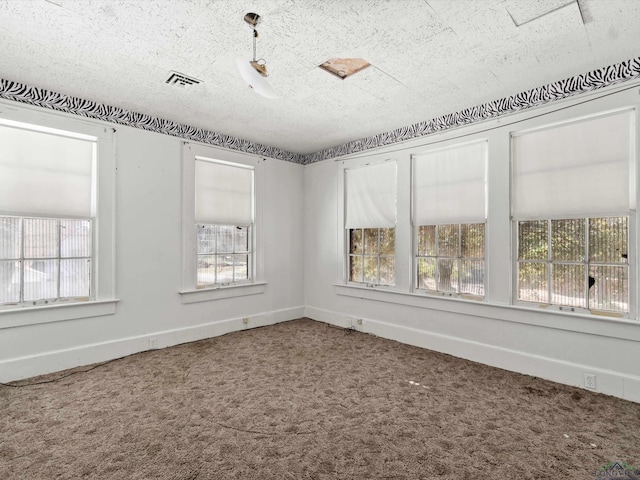 empty room featuring carpet floors, visible vents, a textured ceiling, and baseboards