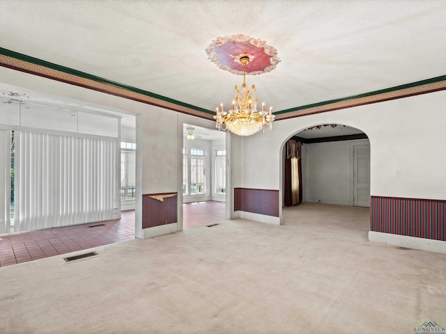 carpeted empty room with visible vents, arched walkways, a wainscoted wall, ornamental molding, and a textured ceiling