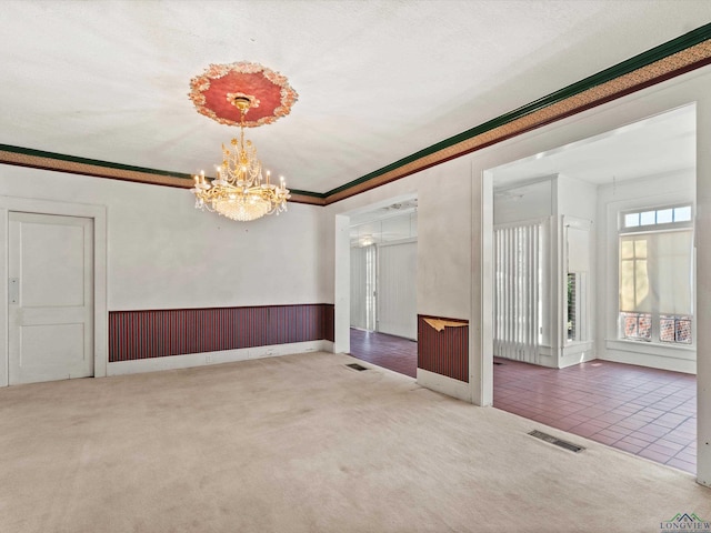 carpeted spare room with a chandelier, a wainscoted wall, visible vents, and crown molding