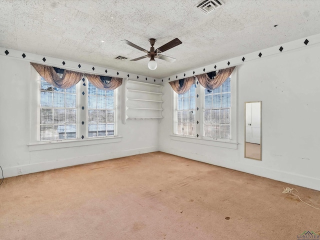 carpeted empty room featuring a textured ceiling, visible vents, and a wealth of natural light