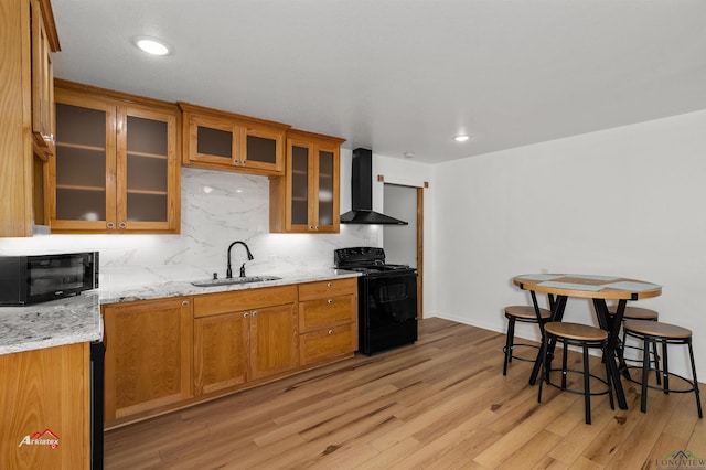 kitchen with light stone countertops, sink, wall chimney range hood, decorative backsplash, and black appliances