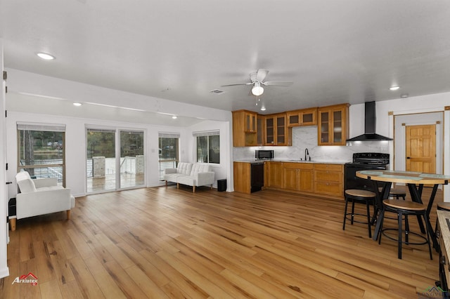 kitchen featuring decorative backsplash, wall chimney exhaust hood, sink, black appliances, and light hardwood / wood-style flooring