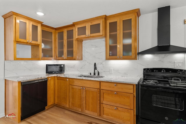 kitchen featuring sink, wall chimney exhaust hood, light stone counters, light hardwood / wood-style flooring, and black appliances