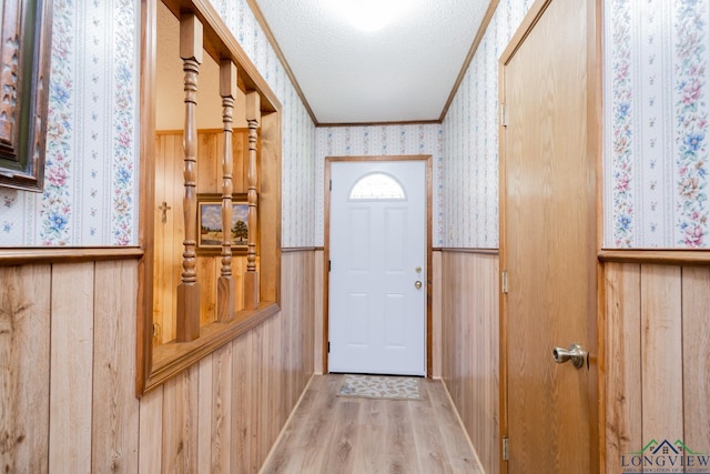 entryway featuring wood walls, light wood-type flooring, a textured ceiling, and ornamental molding