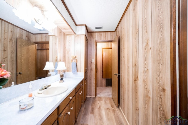 bathroom featuring a textured ceiling, wood-type flooring, vanity, wooden walls, and ornamental molding