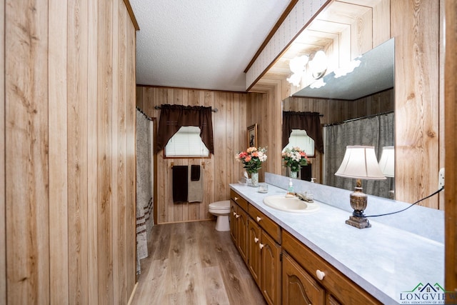 bathroom featuring hardwood / wood-style floors, a textured ceiling, vanity, wooden walls, and toilet