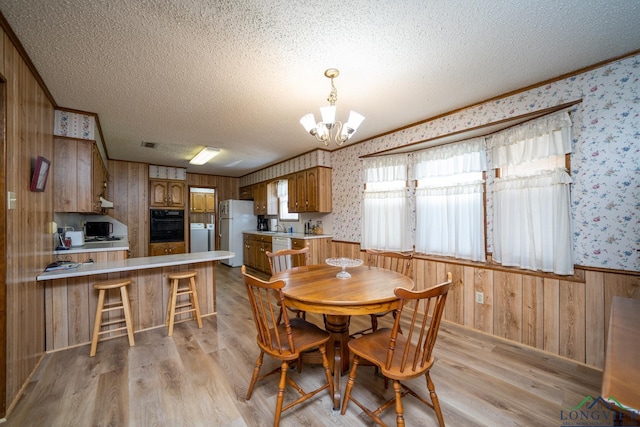 dining room featuring a textured ceiling, a chandelier, light hardwood / wood-style flooring, and washer and dryer