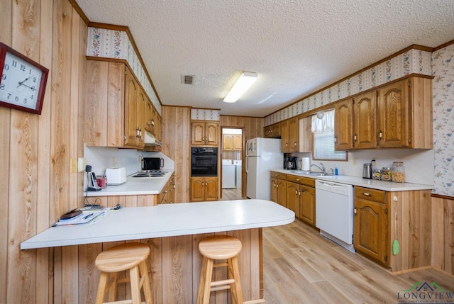 kitchen featuring white appliances, washer / clothes dryer, a textured ceiling, kitchen peninsula, and a breakfast bar