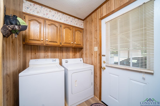 washroom with cabinets, a textured ceiling, washer and clothes dryer, and wood walls