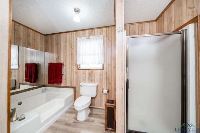 bathroom featuring toilet, a textured ceiling, hardwood / wood-style flooring, wooden walls, and separate shower and tub