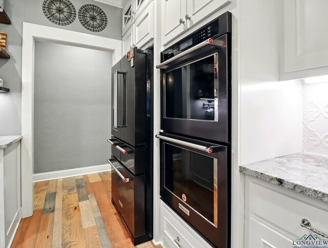 kitchen featuring light stone counters, light wood-style floors, dobule oven black, and white cabinetry