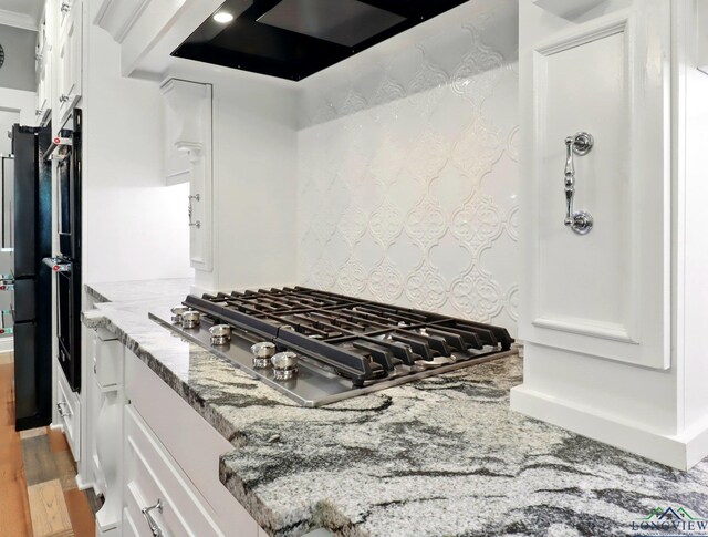 kitchen featuring stainless steel gas cooktop, range hood, light wood-style flooring, light stone counters, and white cabinetry
