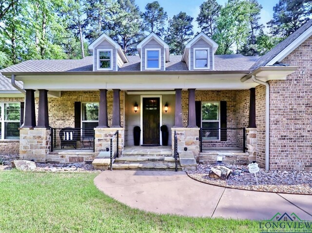 view of front facade with brick siding, a porch, a front yard, and roof with shingles