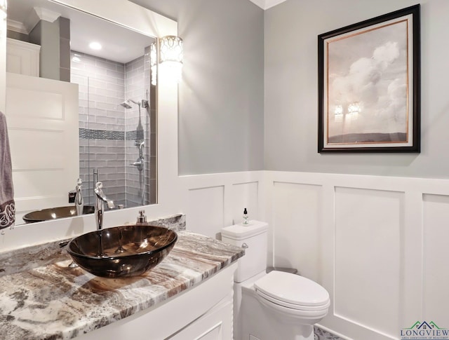 full bath with tiled shower, toilet, a decorative wall, vanity, and wainscoting