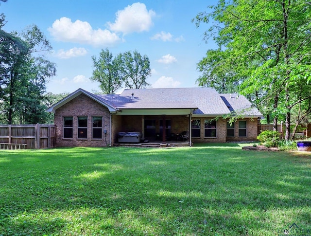 back of house with fence, a lawn, brick siding, and a hot tub