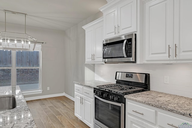 kitchen featuring appliances with stainless steel finishes, pendant lighting, white cabinets, backsplash, and light hardwood / wood-style flooring