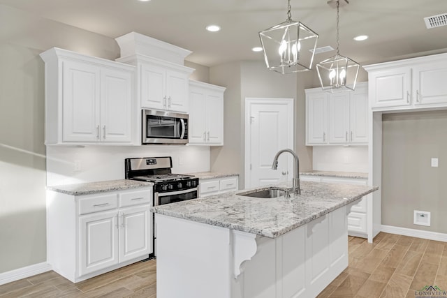 kitchen with white cabinetry, appliances with stainless steel finishes, sink, and a center island with sink