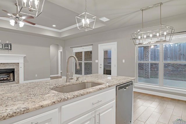 kitchen featuring pendant lighting, sink, dishwasher, white cabinets, and a stone fireplace