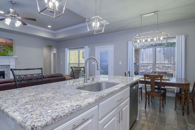 kitchen with sink, an island with sink, white cabinets, a stone fireplace, and decorative light fixtures