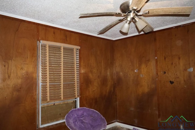 interior space with ceiling fan, wooden walls, crown molding, and a textured ceiling