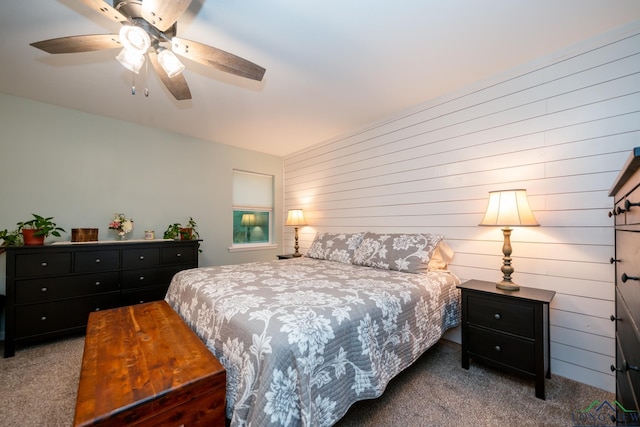 carpeted bedroom featuring ceiling fan and wood walls