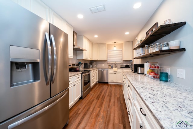 kitchen featuring dark wood-type flooring, white cabinets, wall chimney exhaust hood, light stone countertops, and appliances with stainless steel finishes