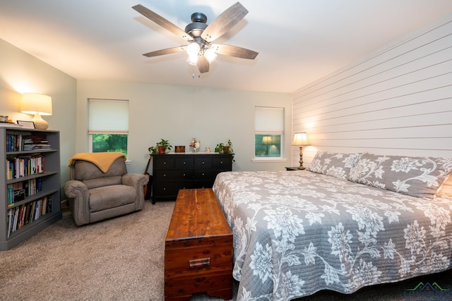 bedroom with carpet flooring, ceiling fan, and wooden walls