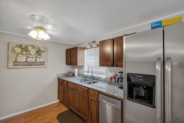 kitchen with light stone countertops, sink, light hardwood / wood-style flooring, appliances with stainless steel finishes, and ornamental molding