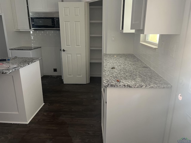 2808 Park Dr, Marshall, TX 75670 - kitchen featuring stainless steel microwave, dark wood-style flooring, decorative backsplash, and white cabinetry