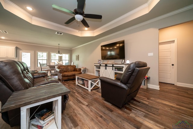 living room with a tray ceiling, ceiling fan, dark wood-type flooring, and ornamental molding