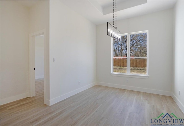 unfurnished dining area with a raised ceiling and light hardwood / wood-style floors