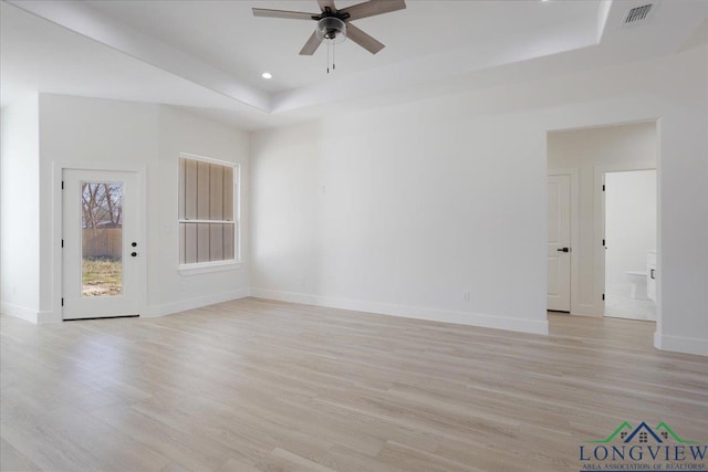 spare room with a tray ceiling, ceiling fan, and light wood-type flooring