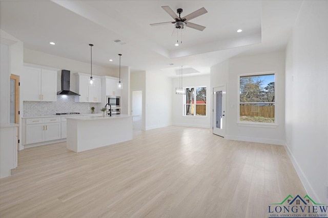 unfurnished living room featuring sink, a tray ceiling, ceiling fan, and light wood-type flooring