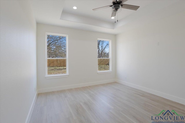 empty room with a raised ceiling, ceiling fan, and light hardwood / wood-style flooring