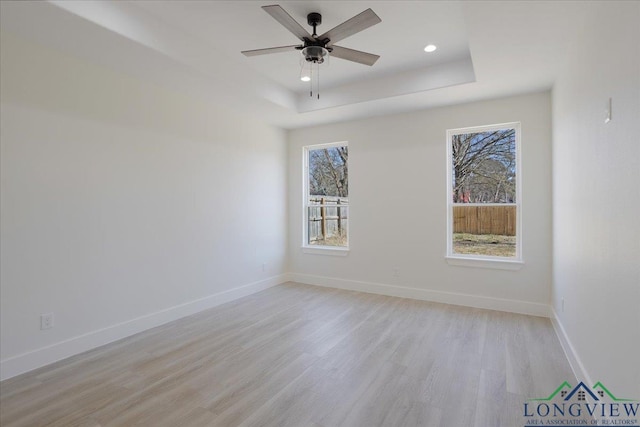 empty room featuring ceiling fan, a tray ceiling, and light wood-type flooring