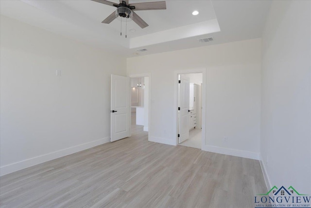 unfurnished bedroom with light hardwood / wood-style flooring, connected bathroom, ceiling fan, and a tray ceiling