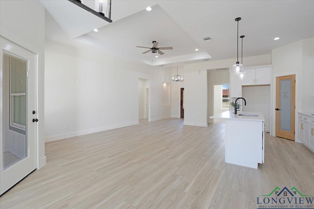 kitchen featuring sink, a tray ceiling, an island with sink, pendant lighting, and white cabinets