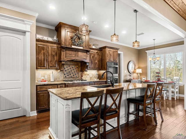 kitchen featuring a large island with sink, light stone countertops, pendant lighting, and a kitchen breakfast bar