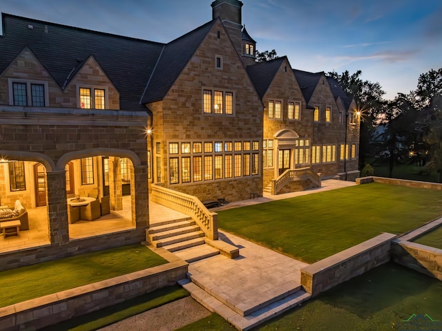 back house at dusk featuring a lawn and a patio area