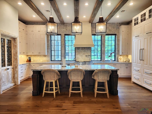 kitchen featuring beam ceiling, a large island with sink, light stone countertops, and white cabinets