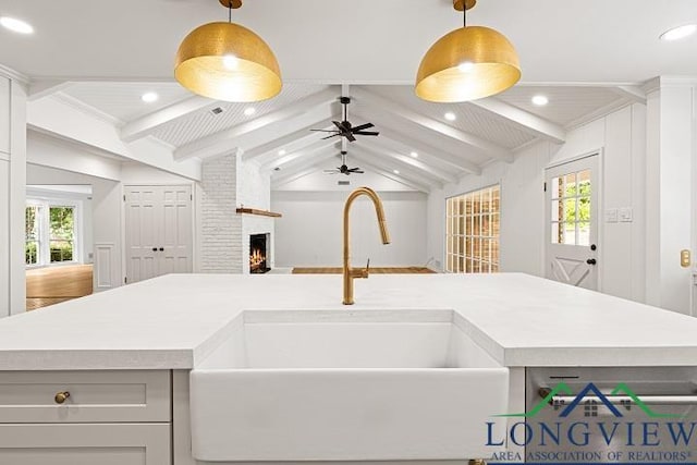 kitchen with vaulted ceiling with beams, ceiling fan, sink, and a fireplace