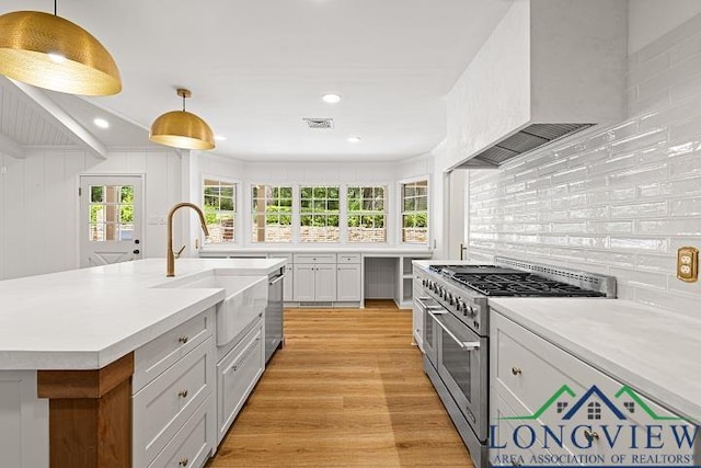 kitchen with pendant lighting, stainless steel appliances, a kitchen island with sink, and wall chimney exhaust hood