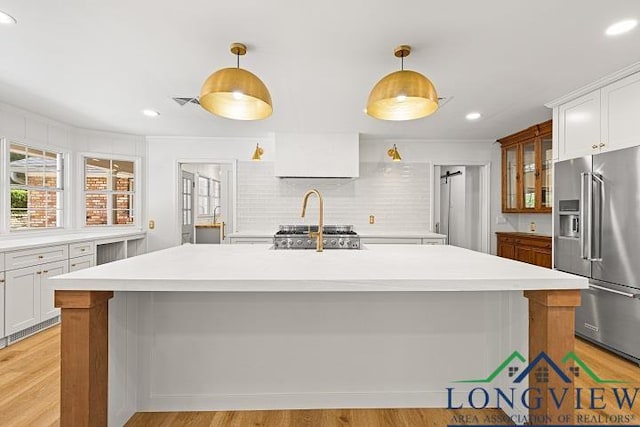 kitchen featuring white cabinets, pendant lighting, high quality fridge, and a kitchen island with sink